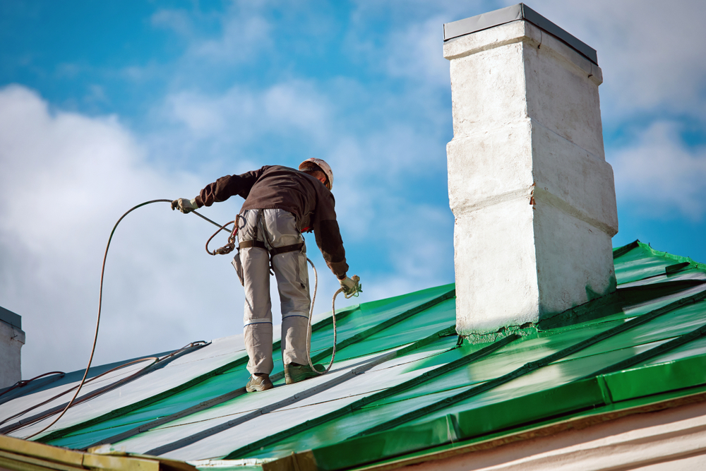 Pracovník společnosti Industrial Alpinist Services natírá střechu zelenou barvou pomocí stříkací pistole. Pracovník společnosti Industrial Alpinist Services natírá střechu zelenou barvou pomocí stříkací pistole